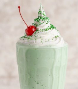 green milkshake with whipped cream and green sprinkles topped with a cherry